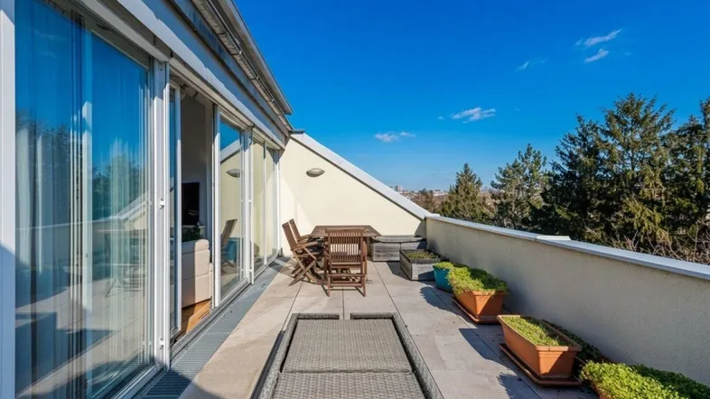 Sonnige Dachterrasse mit Holztisch, Stühlen und Pflanzen, bietet einen weiten Blick ins Grüne.
