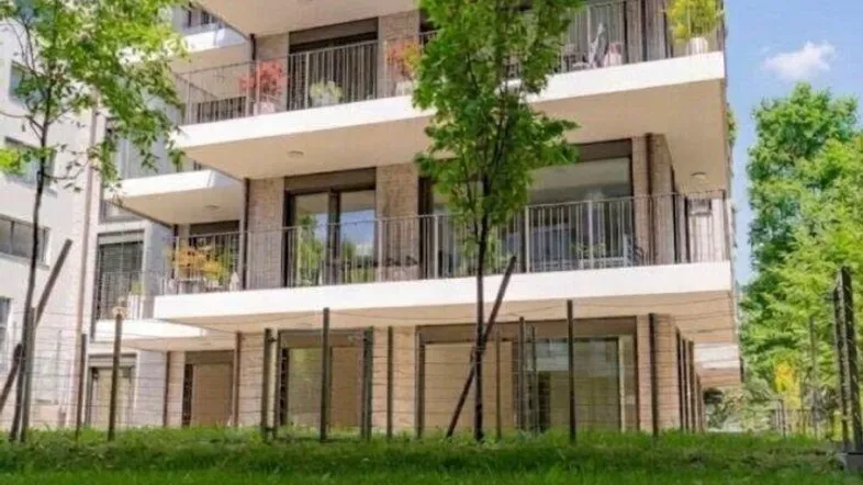 Modernes Mehrfamilienhaus mit Balkonen und Dachterrasse, umgeben von Grünflächen.