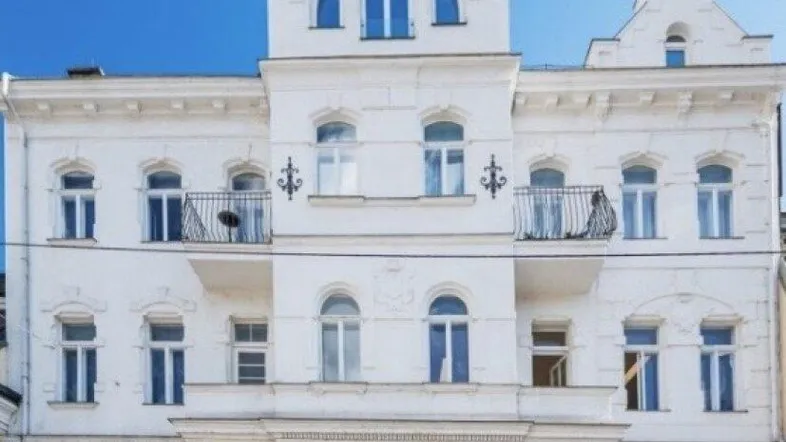 Weißes Altbaugebäude mit dekorativer Fassade, Balkonen und blauer Himmel.