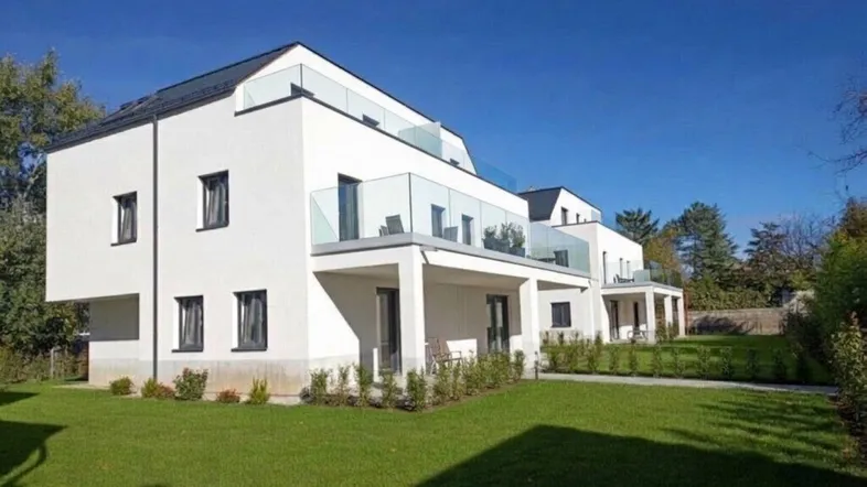 Moderne weiße Gebäude mit Glasbalkonen und gepflegtem Rasen in sonniger Umgebung.