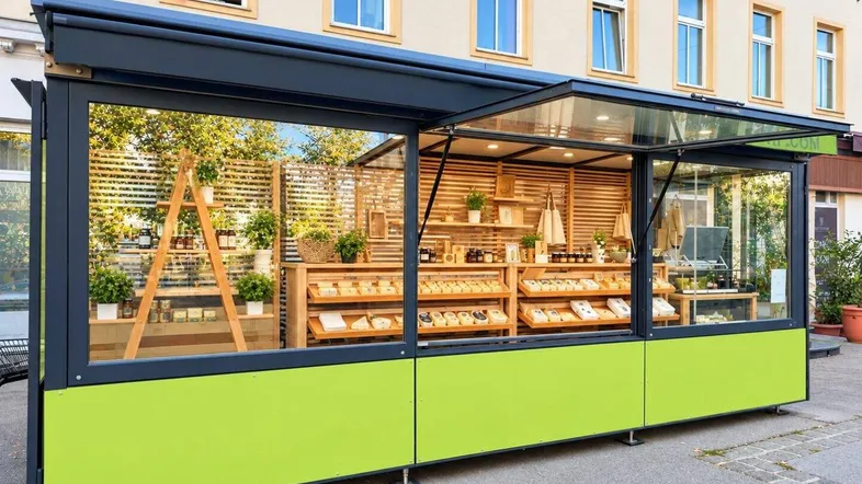 Moderner Verkaufsstand mit großen Glasfenstern und hellgrüner Verkleidung, der Backwaren und andere Produkte präsentiert.