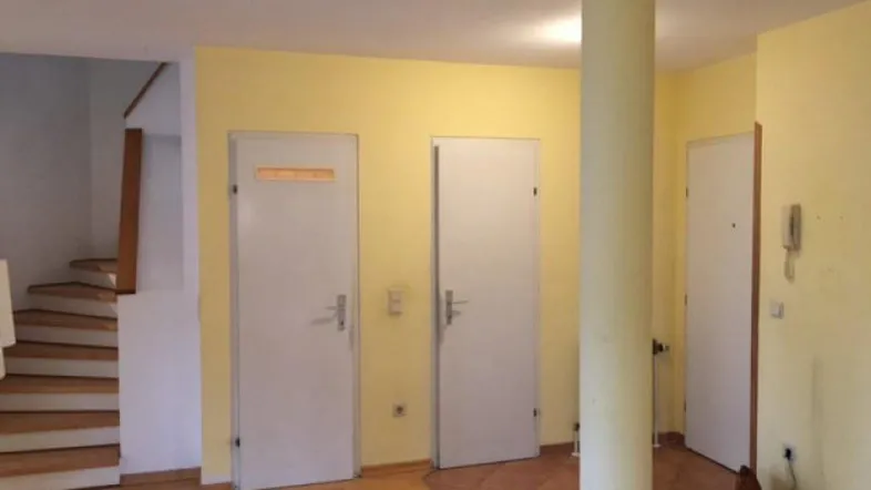 Heller Flur mit Holztreppe, mehreren Türen und gelben Wänden, der verschiedene Bereiche verbindet.