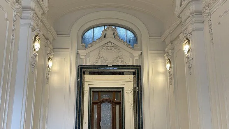 Prunkvoller Eingangsbereich mit hohen Decken, kunstvollen Stuckverzierungen und eleganten Fliesenböden in einem historischen Gebäude.