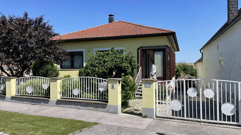 Gelbes Einfamilienhaus mit rotem Ziegeldach, Vorgarten und weißem Gartentor.