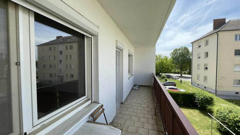 Langer Balkon mit Fliesenboden, kleinem Tisch und Blick auf die umliegenden Gebäude und Grünflächen.