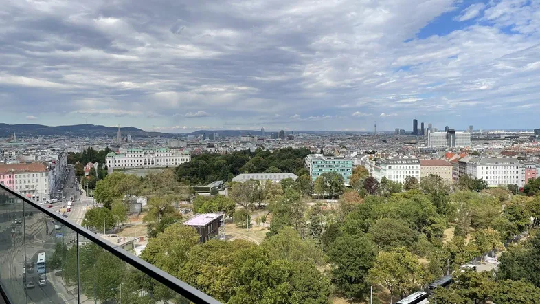 Panoramablick über die Stadt Wien mit grünen Parks und historischer Architektur unter bewölktem Himmel.