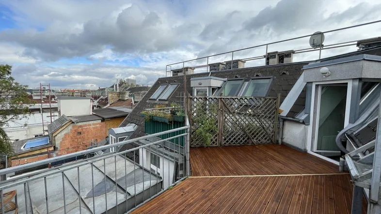 Große Holzterrasse mit Blick über die Dächer der Stadt und einem Metallgeländer.