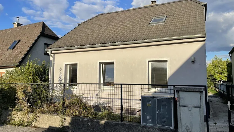 Einfamilienhaus mit Satteldach, Dachfenster und gepflegter Fassade unter blauem Himmel.