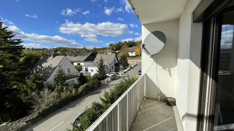 Geräumiger Balkon mit Satellitenschüssel und Blick auf die umliegende Wohngegend unter blauem Himmel.