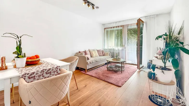 Helles Wohn- und Esszimmer mit Holzboden, rosa Teppich und Zugang zum Balkon.