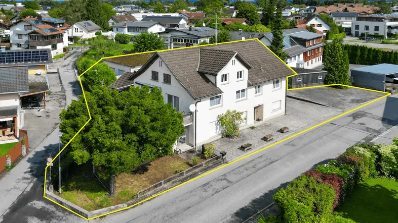 Luftaufnahme eines Einfamilienhauses mit Grundstücksgrenzen in einer Wohnsiedlung mit Bergblick.