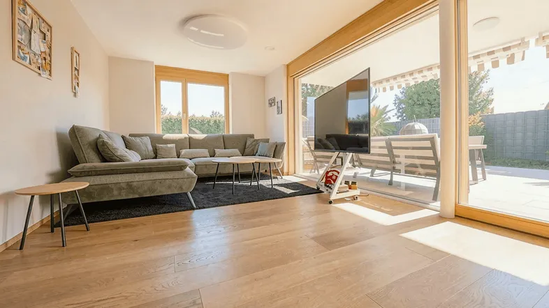 Helles Wohnzimmer mit großem Sofa, Holzboden und Zugang zur Terrasse.