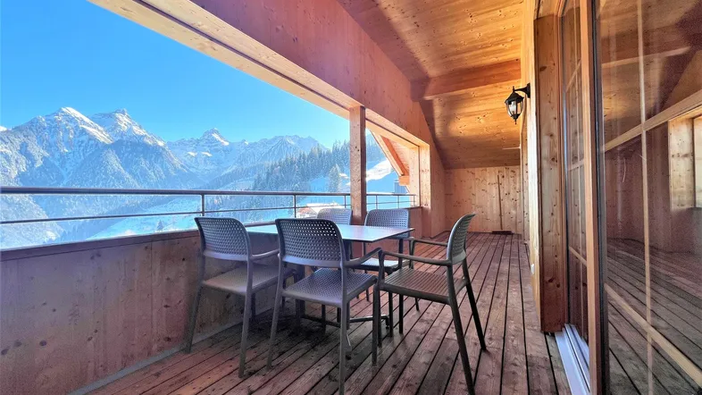 Geräumiger Holzbalkon mit Sitzgelegenheiten und atemberaubendem Blick auf die verschneiten Berge.