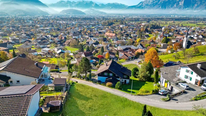 Panoramablick über eine ländliche Siedlung mit Bergen im Hintergrund und herbstlicher Vegetation.