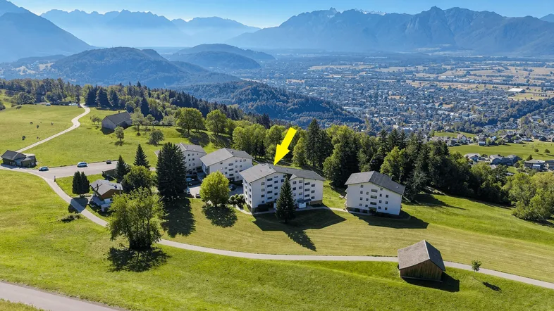 Luftaufnahme der Wohngebäude in einer grünen Hügellandschaft mit Bergen im Hintergrund.