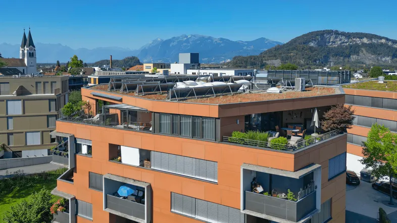 Moderne Wohnanlage mit großer Dachterrasse, Bergblick und Solaranlagen auf dem Dach.