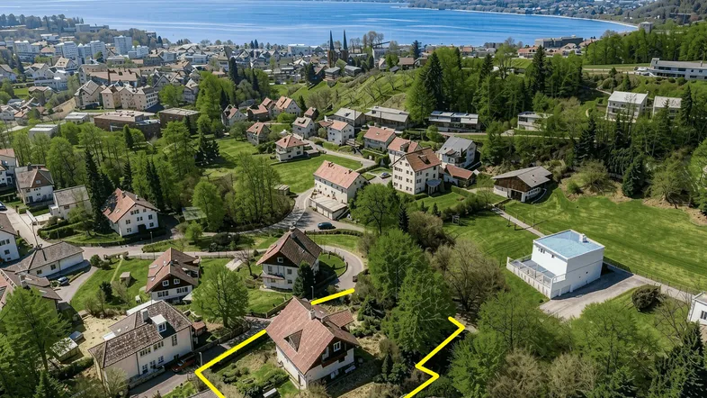 Luftaufnahme des Grundstücks mit See im Hintergrund und umliegender Wohnbebauung in grüner Landschaft.