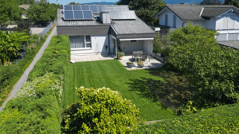 Luftaufnahme eines Einfamilienhauses mit gepflegtem Garten, Terrasse und Solaranlage auf dem Dach.