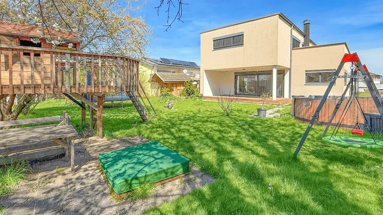 Großer Garten mit Spielplatz, Baumhaus und Whirlpool, umgeben von viel Grün und einem modernen Haus.