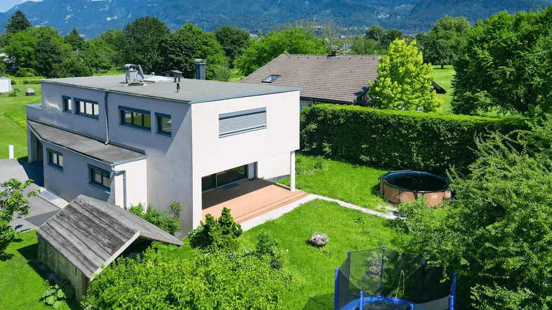 Modernes Haus mit Flachdach, großer Holzterrasse und weitläufigem Garten mit Bergblick.