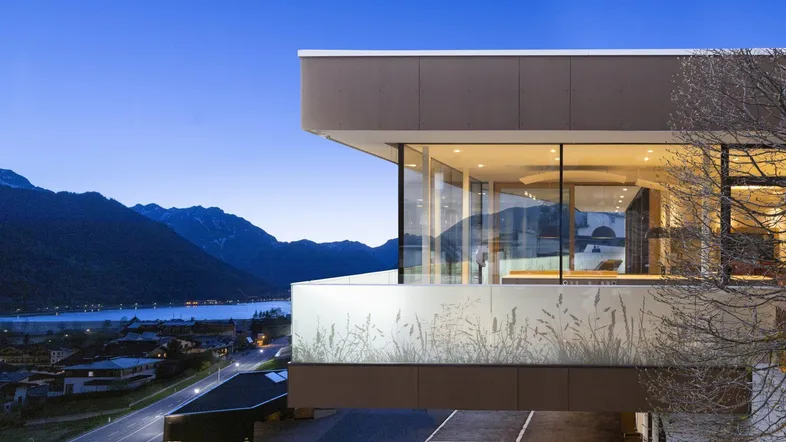 Moderne Architektur mit großen Glasfronten und Panoramablick auf See und Berge bei Dämmerung.
