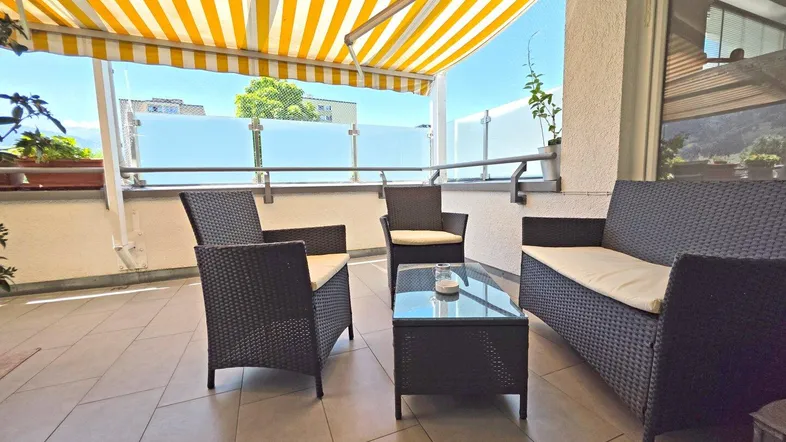 Geräumige Terrasse mit bequemen Loungemöbeln und einer gelb-weiß gestreiften Markise für Sonnenschutz.