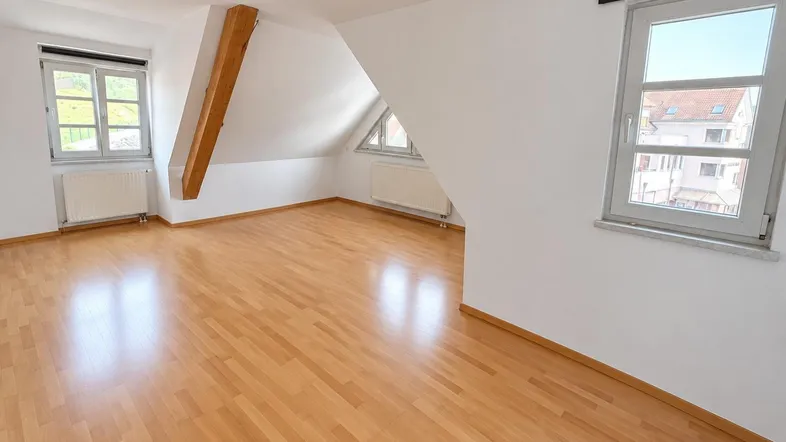 Helles Zimmer im Dachgeschoss mit Holzbalken, Schrägen und Parkettboden, ideal als Wohn- oder Schlafbereich.