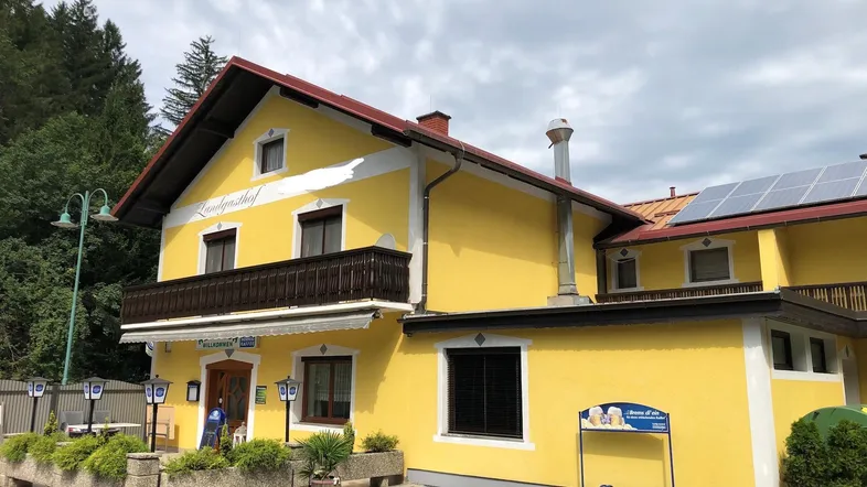 Gelbes Landgasthof-Gebäude mit traditionellem Balkon, Solaranlagen auf dem Dach und einem einladenden Eingangsbereich.