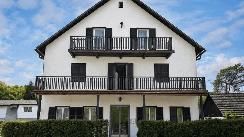 Traditionelles Wohnhaus mit weißer Fassade, schwarzen Fensterläden und mehreren Balkonen unter blauem Himmel.