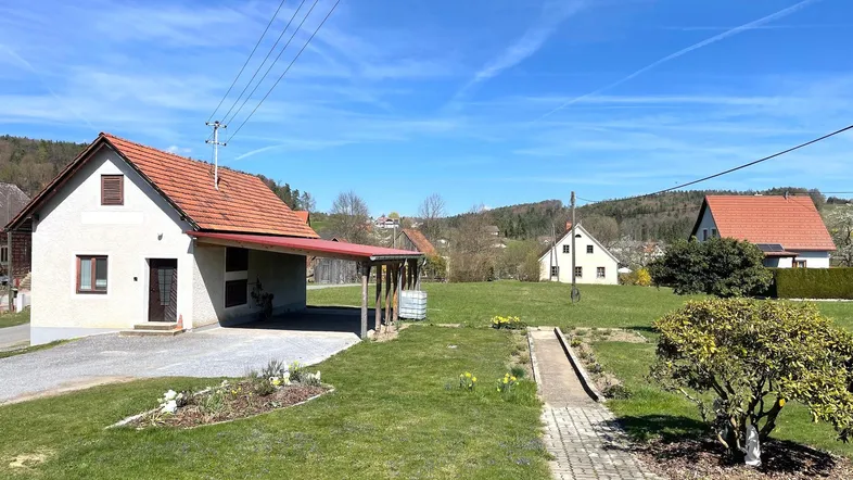 Blick auf das Haus mit Carport, umgeben von einem gepflegten Garten und ländlicher Umgebung.