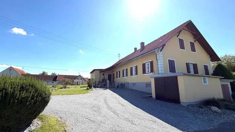 Gelbes Einfamilienhaus mit Satteldach, Kiesauffahrt und gepflegtem Vorgarten unter strahlendem Himmel.