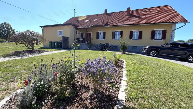 Gelbes Einfamilienhaus mit rotem Ziegeldach, umgeben von einem gepflegten Garten und Rasenfläche.