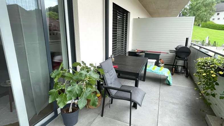 Möblierter Balkon mit Fliesenboden, Grillbereich und Blick ins Grüne.