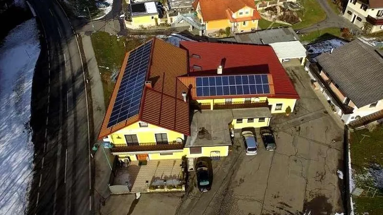 Luftaufnahme eines gelben Gebäudes mit rotem Dach, Solarpaneelen und Parkplatz in ländlicher Umgebung.