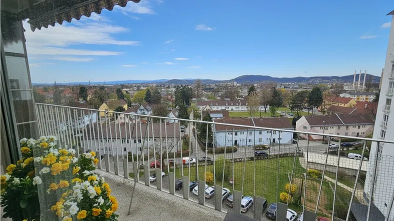 Geräumiger Balkon mit weitem Blick über die Stadt und grüne Umgebung unter blauem Himmel.