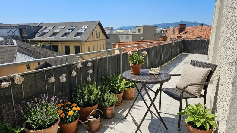 Sonniger Balkon mit Pflanzen, kleinem Tisch und Stühlen, bietet einen weiten Blick über die Stadt.
