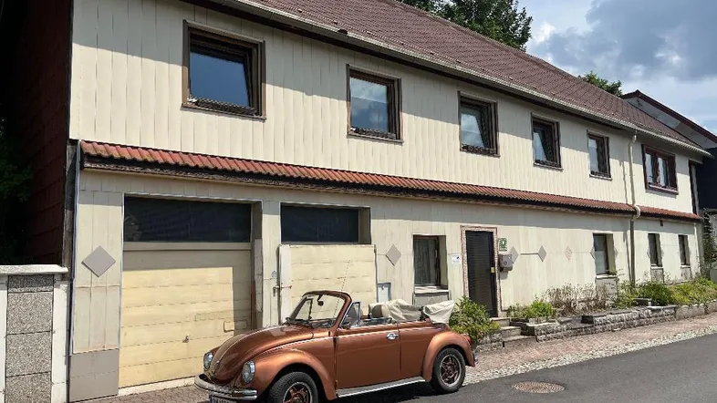 Äußere Ansicht des Hauses mit heller Fassade, braunem Dach und einer Garage an der Vorderseite.