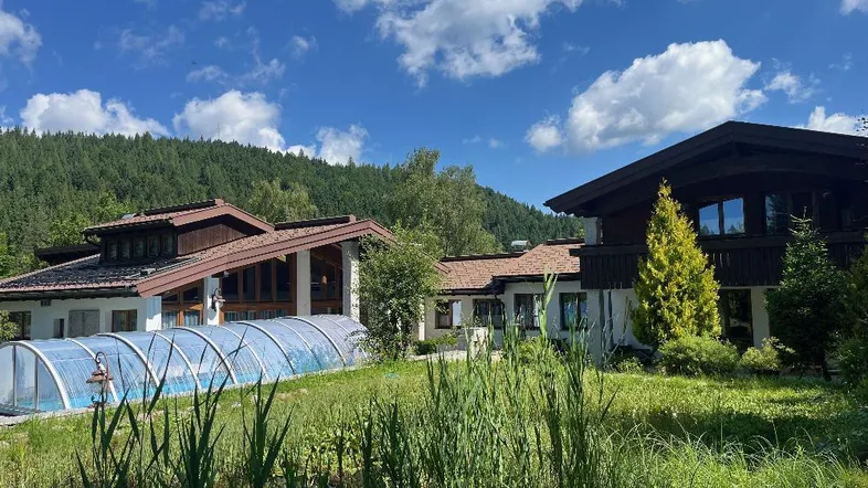 Anwesen mit großem Garten, Teich und überdachtem Pool, umgeben von grünen Wäldern.