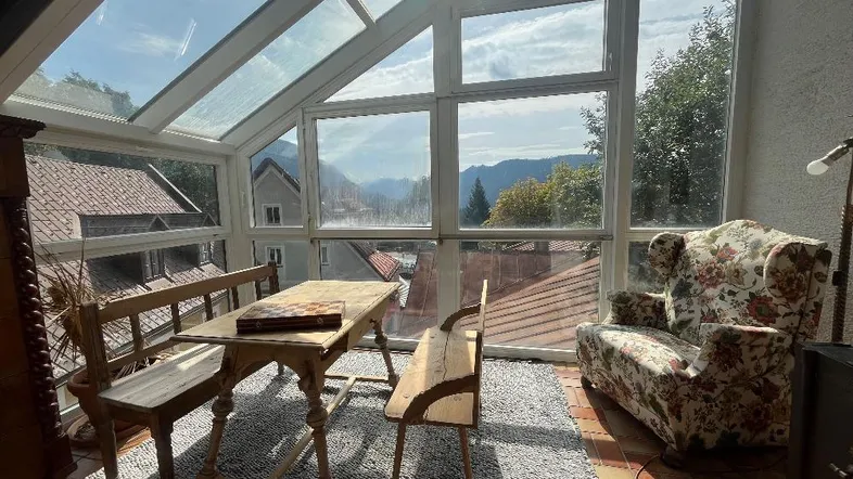 Heller Wintergarten mit großen Glasflächen, Bergblick und traditionellen Möbeln, ideal zum Entspannen.