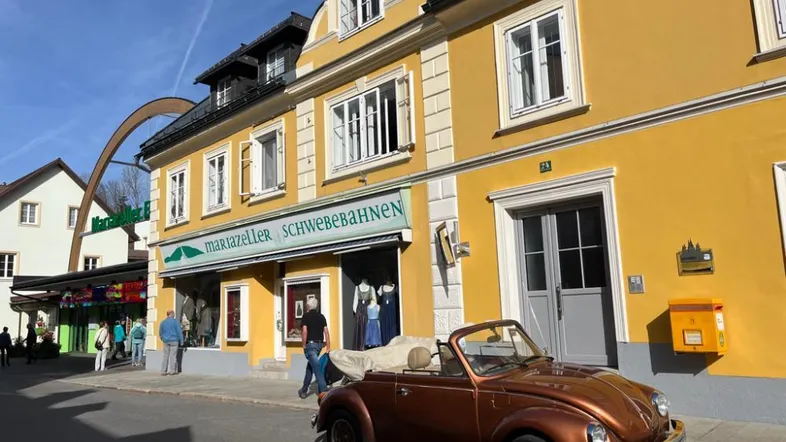 Gelbes Gebäude mit traditioneller Architektur an einer belebten Straße, davor ein klassisches Cabriolet.