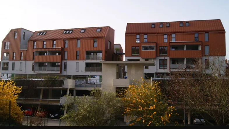 Moderne Wohngebäude mit markanter kupferfarbener Fassade und Balkonen unter hellem Himmel.