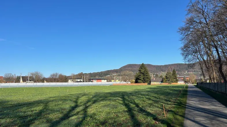 Weitläufiges grünes Feld mit Blick auf die umliegende Landschaft und bewaldete Hügel im Hintergrund.