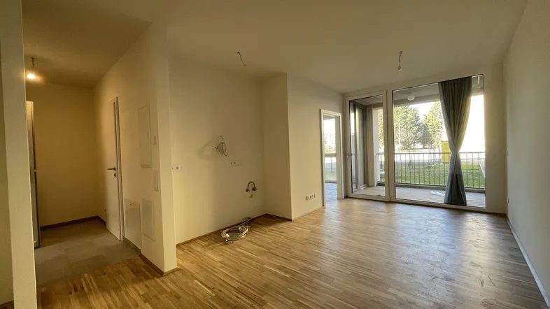 Heller, leerer Wohnbereich mit Parkettboden und Zugang zu einem Balkon oder einer Terrasse.