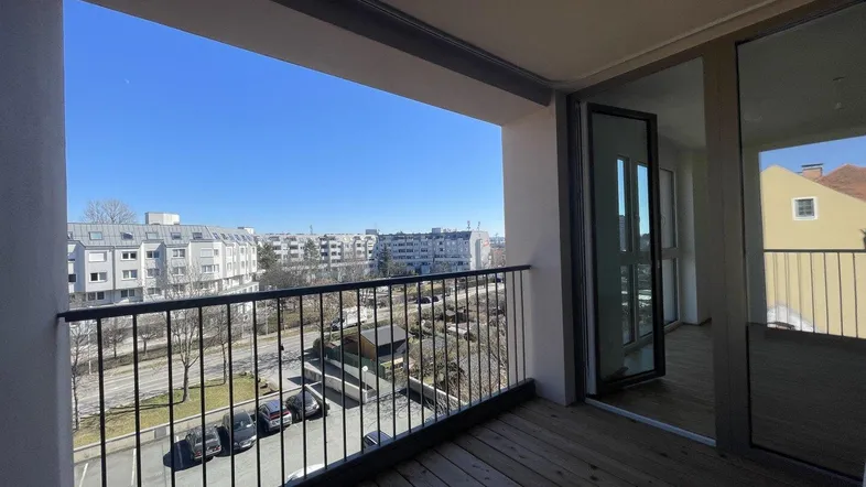 Geräumiger Balkon mit Holzboden und weitem Blick über die Stadt und umliegende Gebäude.
