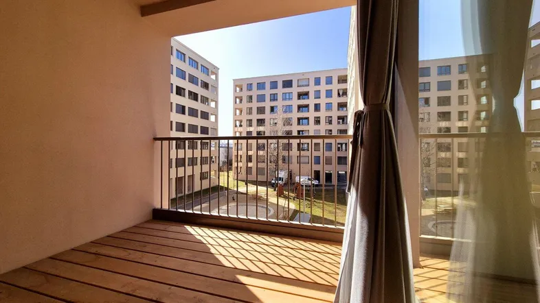 Heller Balkon mit Holzboden und Blick auf moderne Wohngebäude im Innenhof.