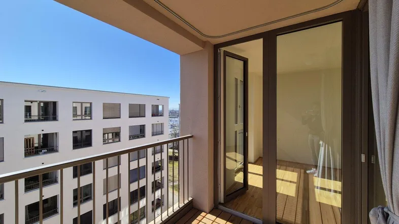 Heller Balkon mit Holzboden und Blick auf die umliegenden Gebäude und den blauen Himmel.