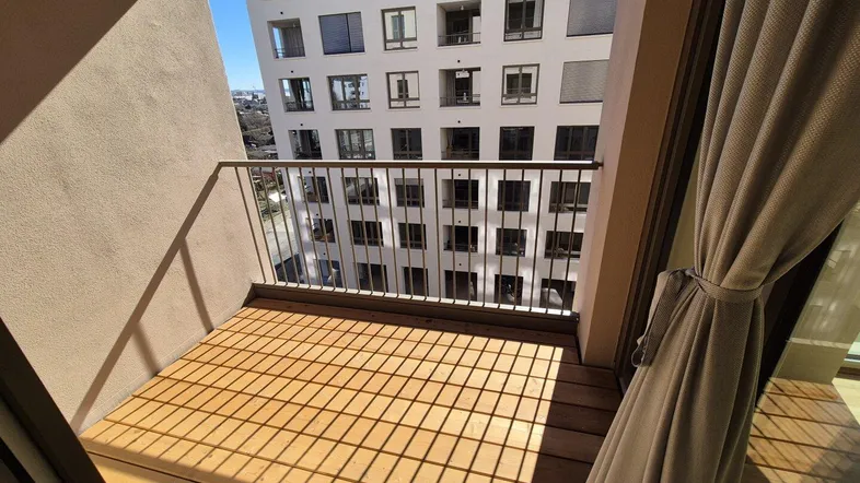 Heller Balkon mit Holzboden und Blick auf das gegenüberliegende moderne Gebäude.