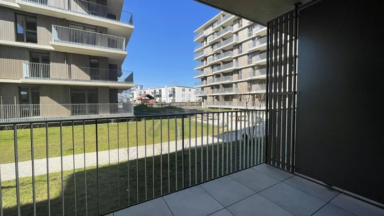 Heller Balkon mit Fliesenboden und Blick auf die umliegenden Neubauten und Grünflächen.