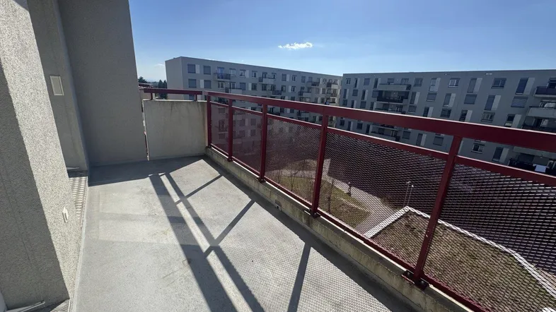 Heller Balkon mit Betonboden und rotem Metallgeländer, bietet Blick auf umliegende Gebäude.