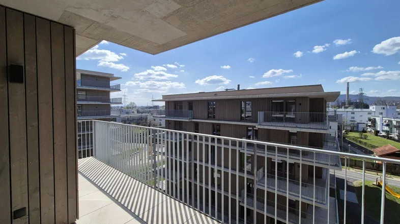 Balkon mit Blick auf moderne Wohngebäude und die Umgebung unter blauem Himmel.